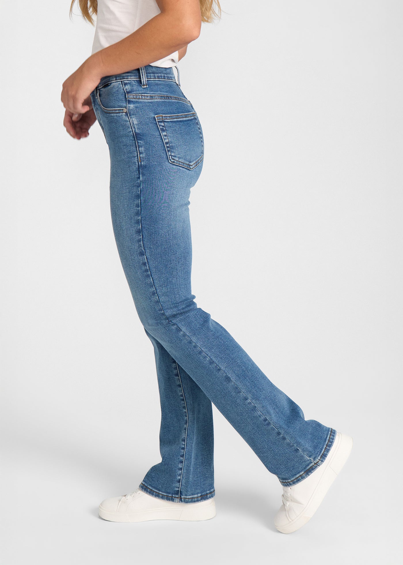 Blå denim bootcut jeans, modelnavn Rivers, som sidder tæt om hofter og lår med et let svaj fra knæet og ned, set fra siden på model.