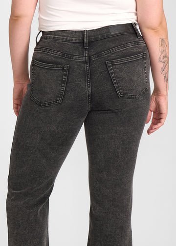 Mørkegrå denim bootcut jeans, modelnavn Shadows, som sidder tæt om hofter og lår med et let svaj fra knæet og ned, set bagfra tæt på for at vise detaljer. på en plus-size model.