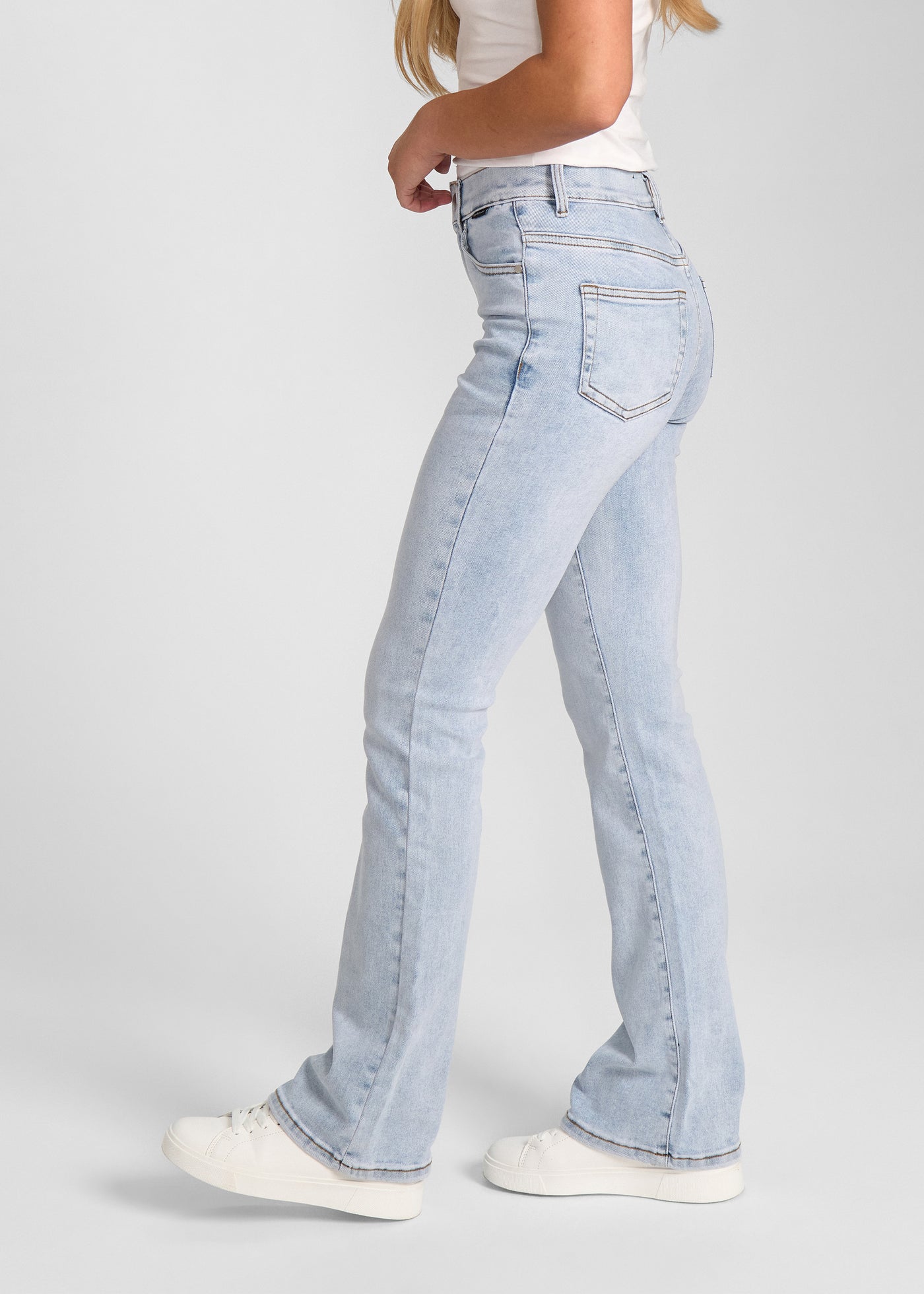 Lyseblå denim bootcut jeans, modelnavn Waves, som sidder tæt om hofter og lår med et let svaj fra knæet og ned, set fra siden på model.
