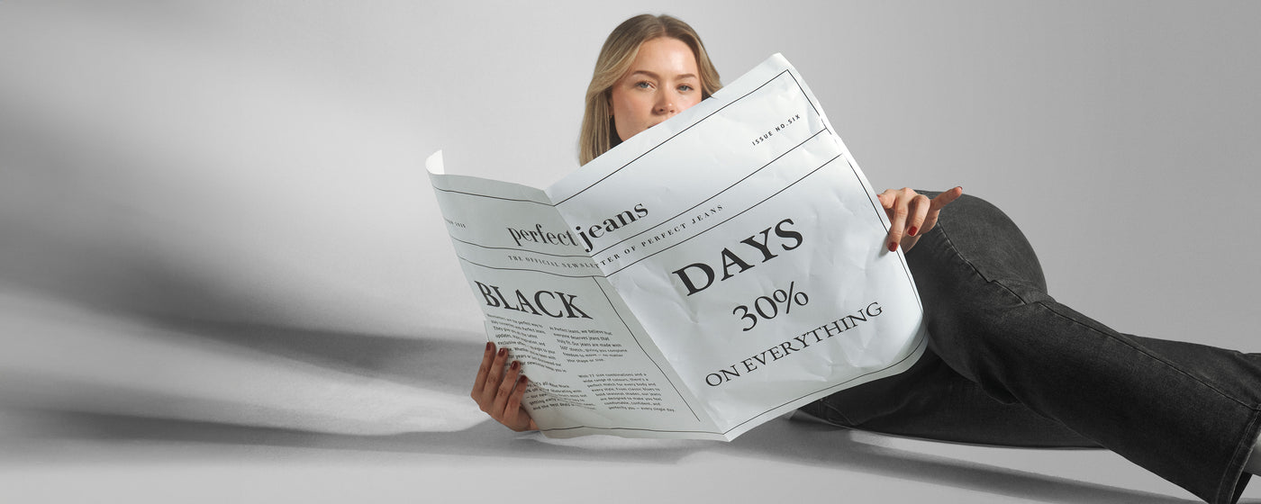 Kvinde i et par mørkegrå denim jeans fra Perfect Jeans, der holder en avis, som annoncerer at der er Black Days med 30% rabat på alt.