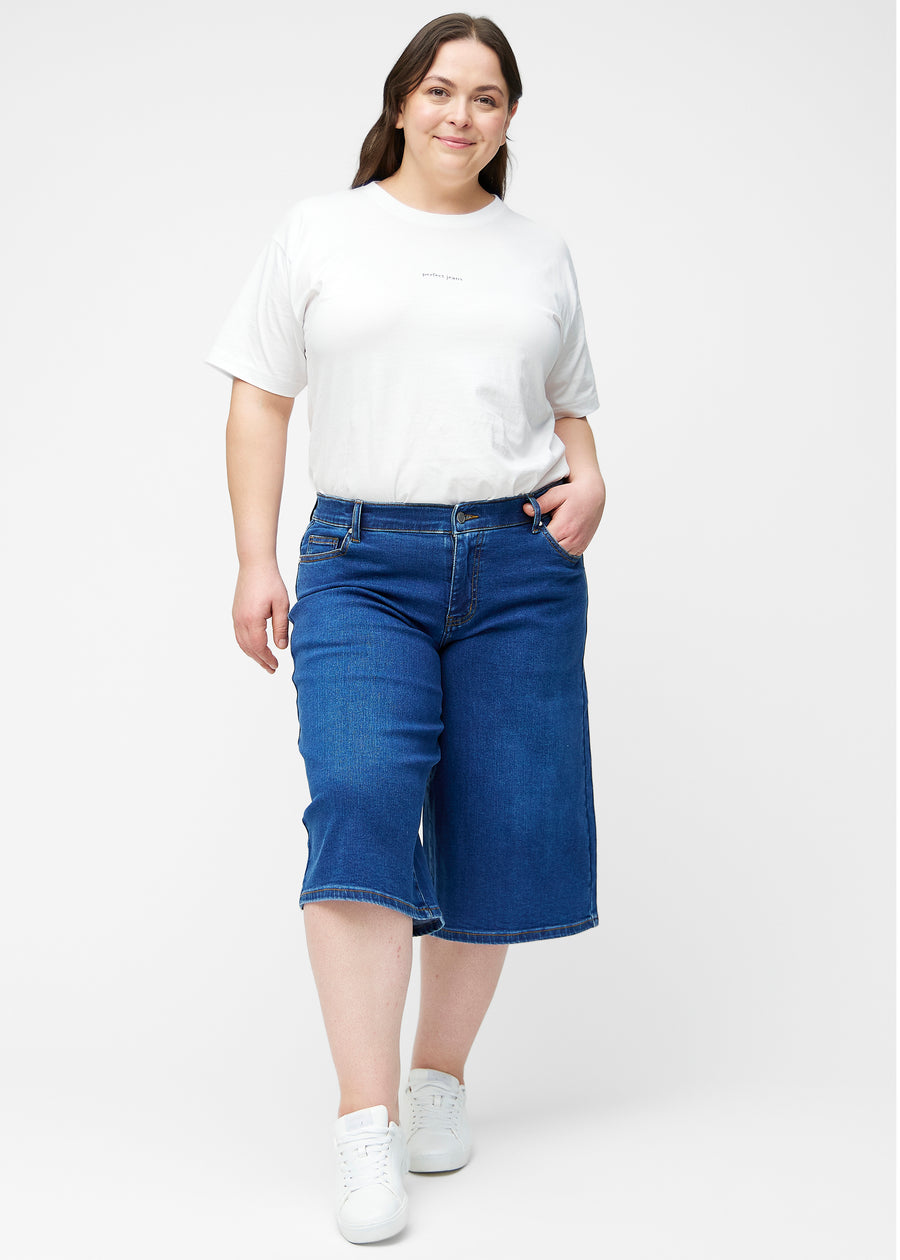 Plus-size model viser løse, mørkeblå denim capris i farven Oceans i bevægelse og demonstrerer pasform og materiale.