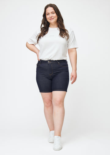 Plus-size model viser dyb mørkeblå denim shorts til kvinder i farven Midnights med skinny pasform i bevægelse.