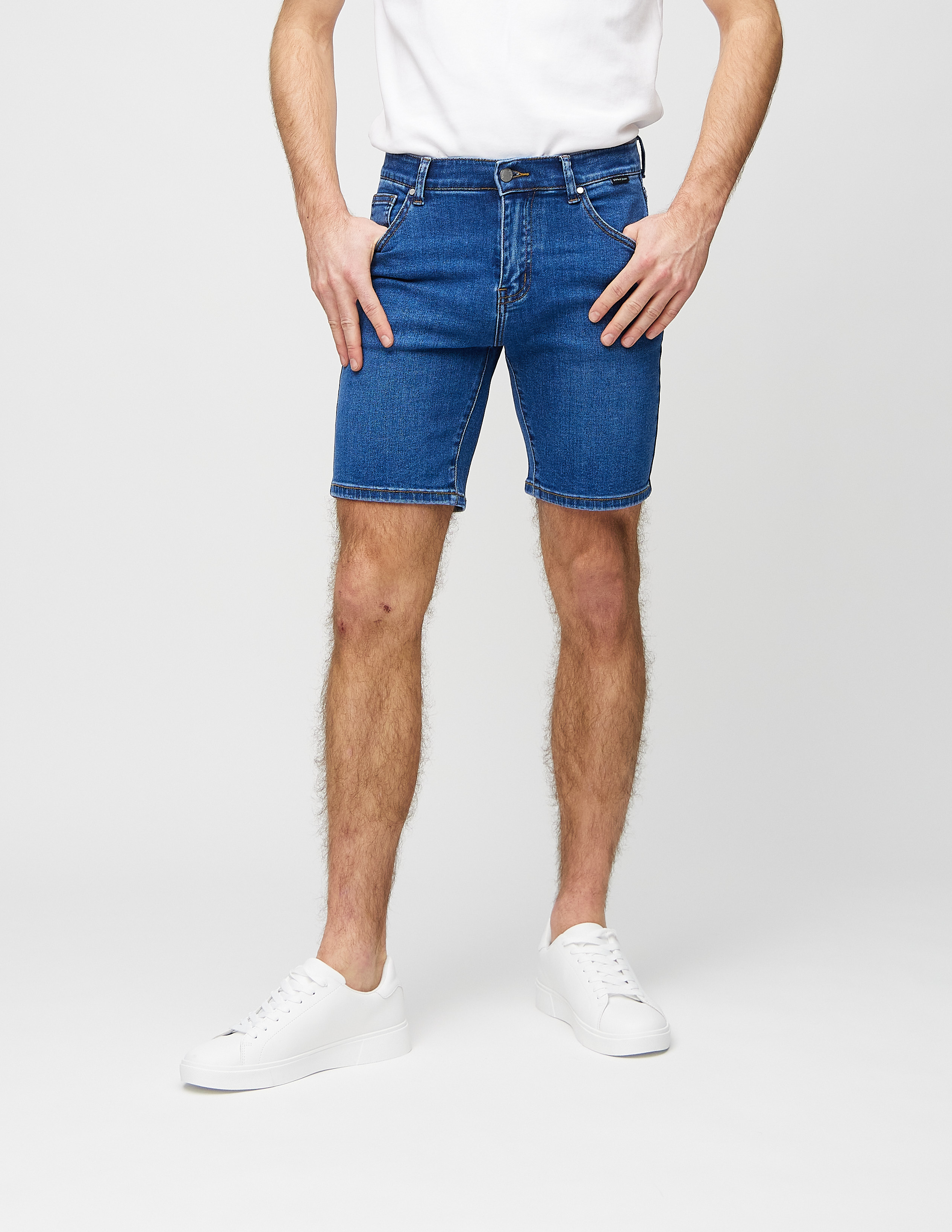 Herremodel med hænderne i lommerne på et par slim denimshorts i den mørkeblå farve Oceans